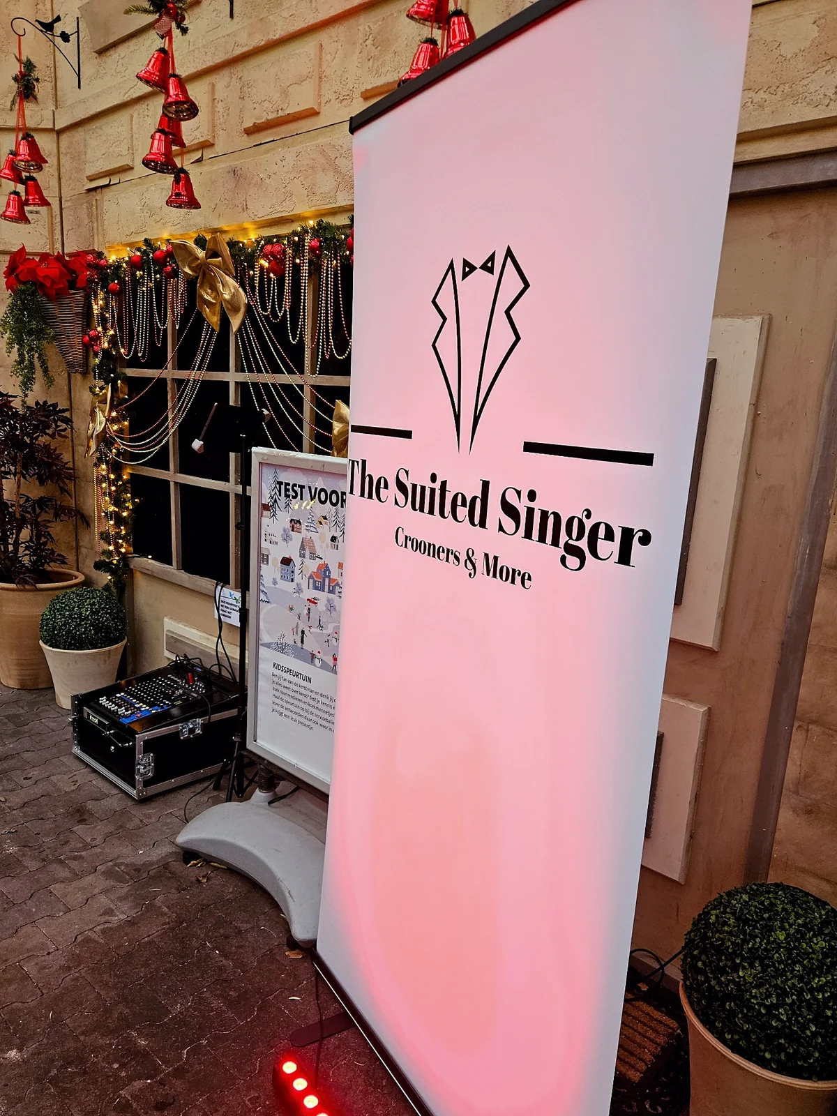 Roll-up banner van The Suited Singer tussen kerstdecoratie, met mengpaneel en flightcase