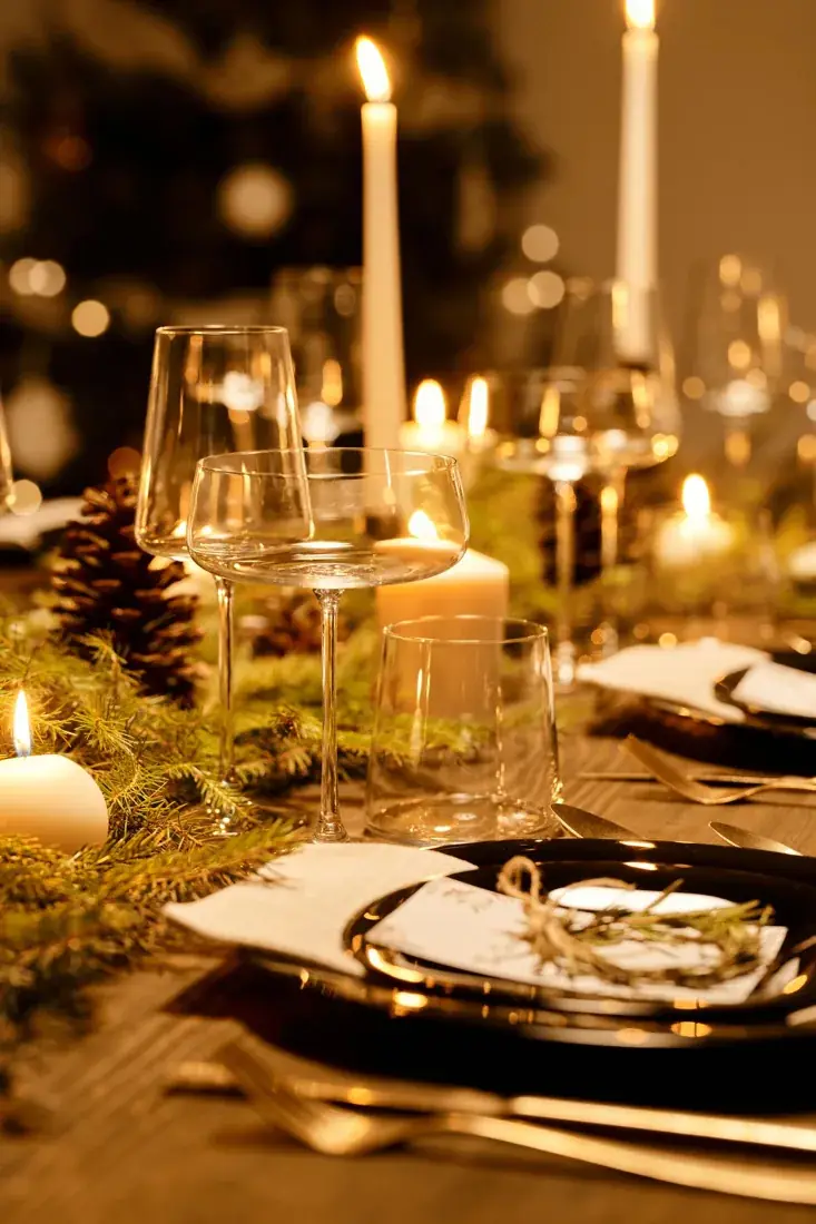 Feestelijk gedekte kersttafel met kaarsen, glazen en groene takken.